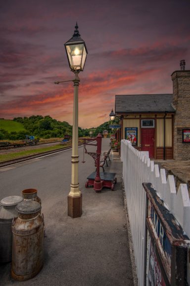 A vintage railway station with a lamp post and a scenic sunset sky.