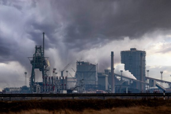 Industrial facility against a dark, cloudy sky, with smokestacks and machinery visible.