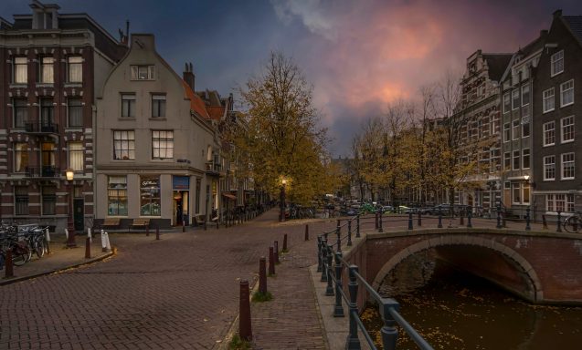 A picturesque canal scene in Amsterdam with autumn trees and bridges at dusk.