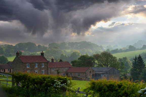 Dramatic cloudy sky over rural cottages and lush green hills.